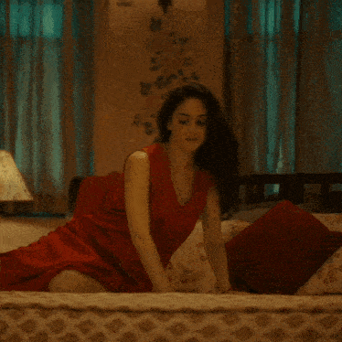 a woman in a red dress is kneeling on a bed in front of a lamp