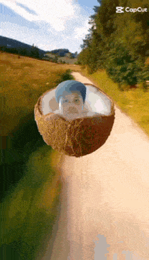 a coconut with a man 's face inside of it is floating on a dirt road .