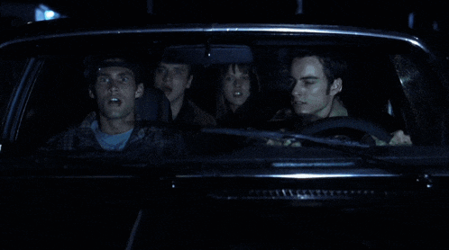a group of people are sitting in a car and one of them is looking at the rear view mirror