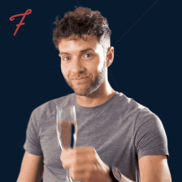 a man in a grey shirt is holding a glass of champagne with the letter f behind him