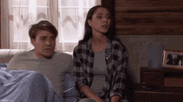 a woman in a plaid shirt sits next to a man in a gray shirt