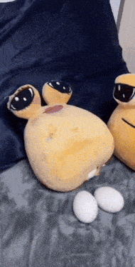 two stuffed animals are laying on a bed next to eggs