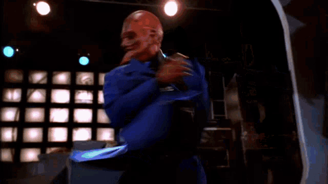 a bald man in a blue suit dancing on a stage