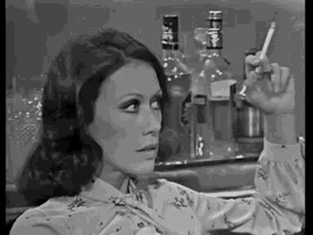 a woman is smoking a cigarette in a black and white photo while sitting at a bar .