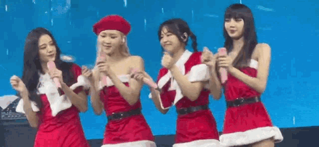 a group of women are standing next to each other on a stage wearing santa claus outfits .