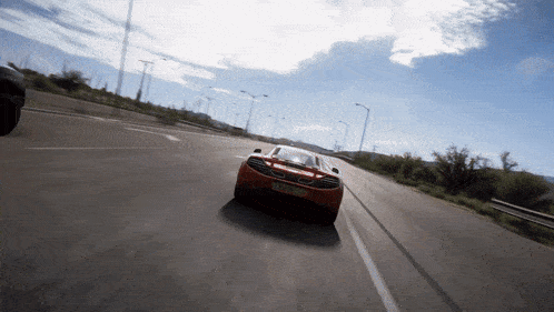 an orange sports car is driving down a road with a license plate that starts with the letter n