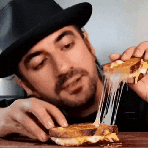 a man in a fedora is eating a grilled cheese sandwich