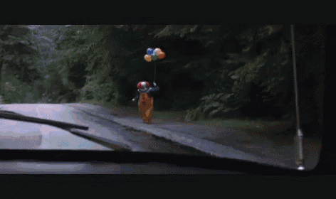 a clown is holding a bunch of balloons on a road .