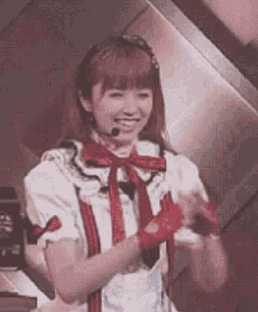 a girl in a white dress with a red bow and gloves is smiling while wearing a microphone .