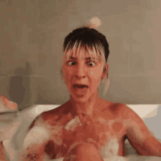 a naked woman is taking a bath in a bathtub and making a funny face