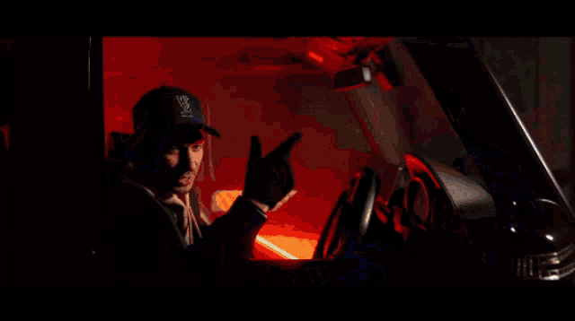 a man wearing a hat is driving a car with red lights behind him
