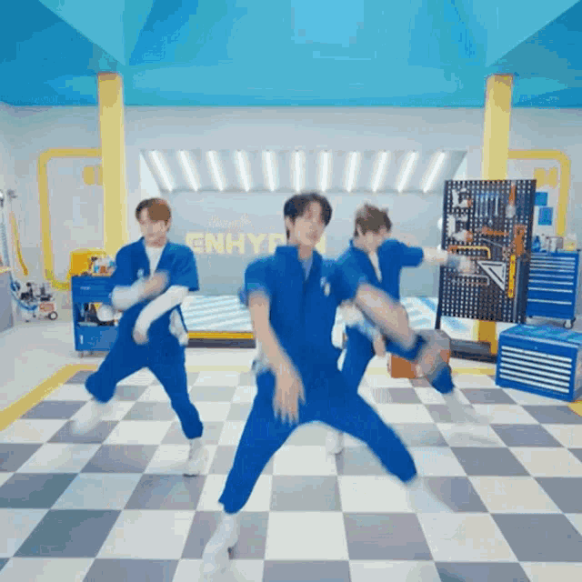 a group of men in blue jumpsuits are dancing in a room with the word enhyp on the wall
