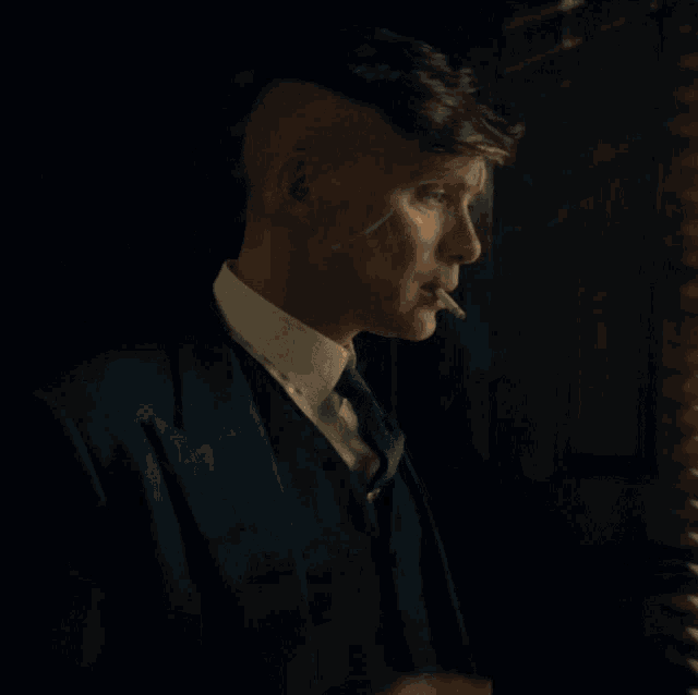 a man in a suit and tie is lighting a cigarette