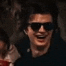 a man wearing sunglasses is smiling and laughing while sitting in a dark room .
