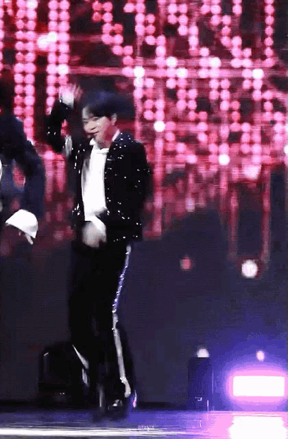 a man in a sequined jacket is dancing on stage