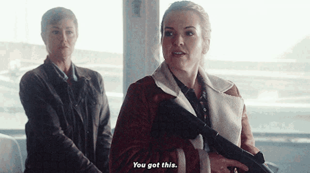 a woman holding a gun says " you got this " in front of another woman