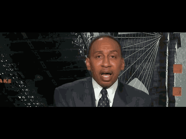 a man in a suit and tie is talking in front of a sign that says " make "