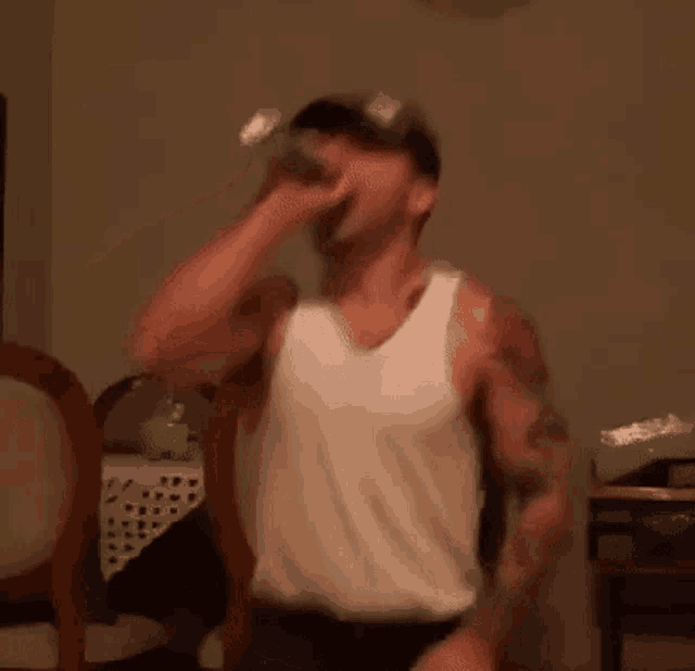 a man in a tank top is drinking from a bottle .