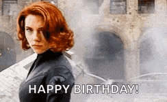 a woman with red hair is standing in front of a building and says happy birthday .