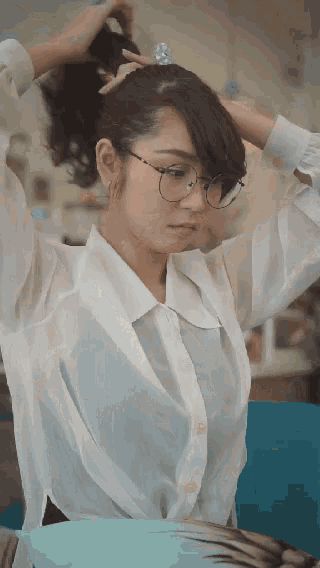 a woman wearing glasses and a white shirt is holding her hair in a ponytail