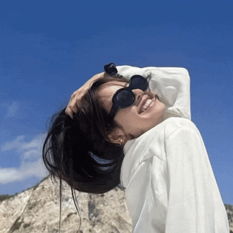 a woman wearing sunglasses and a white shirt looks up at the sky