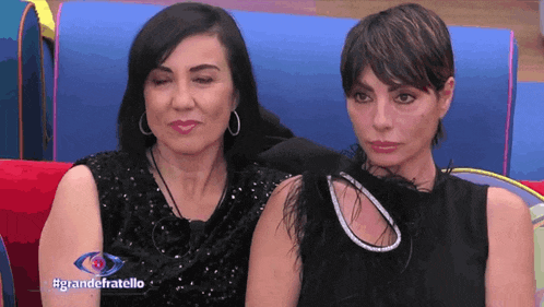 two women are sitting next to each other on a blue couch and the words grandefratello are on the screen