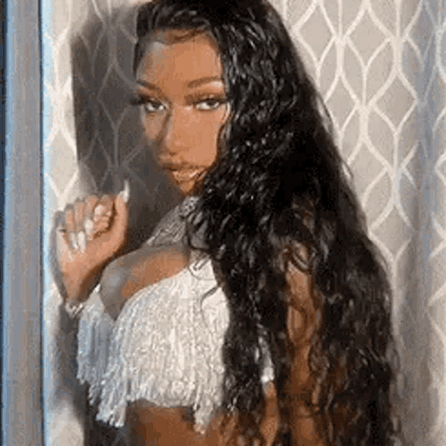 a woman with long hair is standing in front of a window wearing a white top .