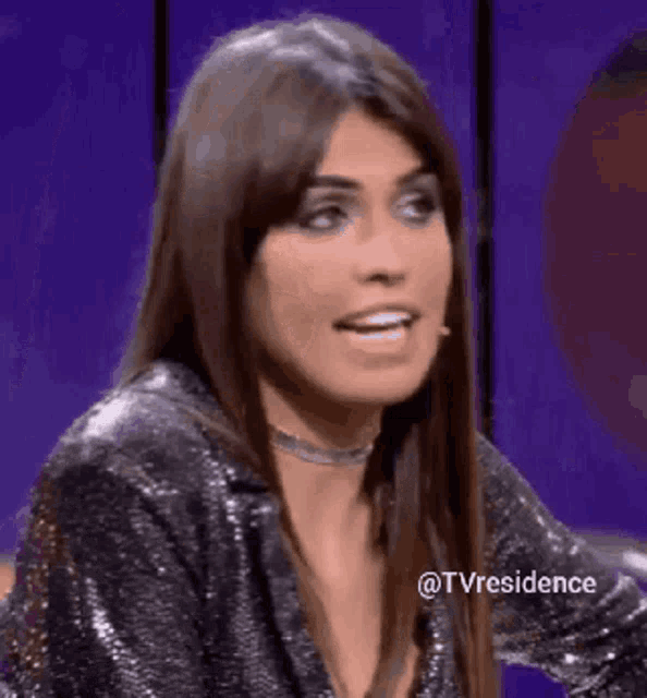 a woman is blowing a kiss while wearing a sequined jacket and choker .