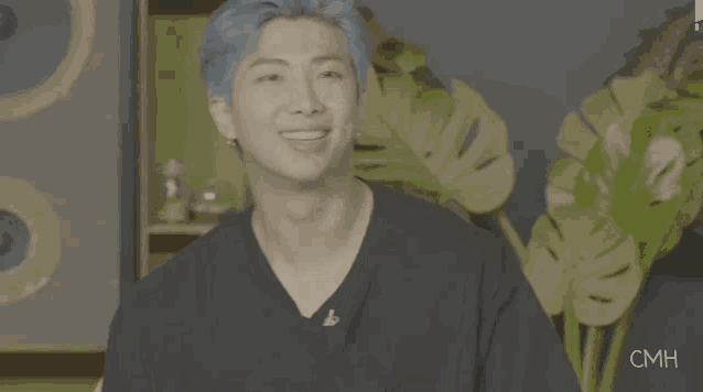 a man with blue hair is wearing a black shirt and pointing his finger at something .