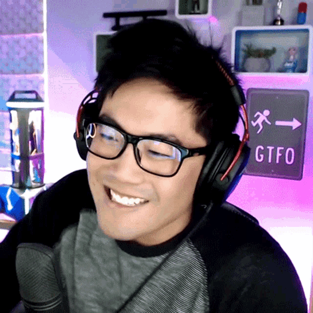 a man wearing glasses and headphones stands in front of a sign that says gtfo