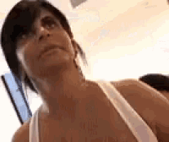 a woman is wearing a white tank top and looking up .