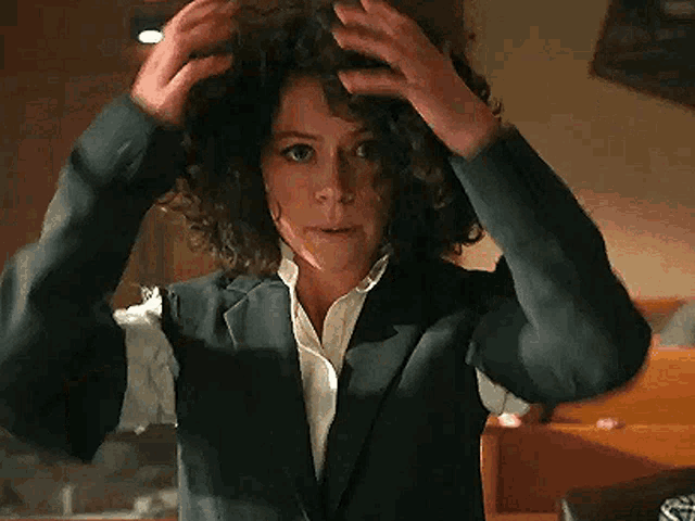 a woman with curly hair is wearing a suit and adjusting her hair .