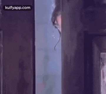 a woman is peeking out of a doorway and looking at the camera .