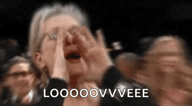 a woman is screaming in a crowd of people while covering her face with her hands .