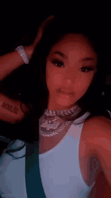 a woman wearing a white tank top and a necklace is taking a selfie .