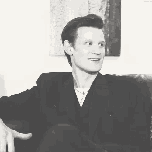 a man in a suit is smiling in a black and white photo with the word vogue on the bottom
