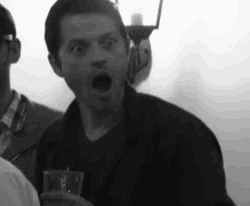 a black and white photo of a man holding a glass and making a funny face .