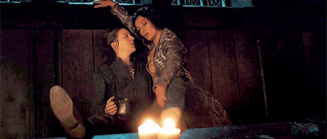 two women are sitting at a table with candles and one of them is holding another woman 's arm .