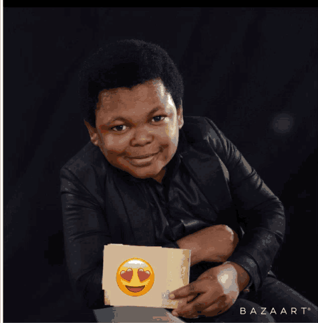a boy in a black jacket is holding a piece of paper with a heart emoji on it