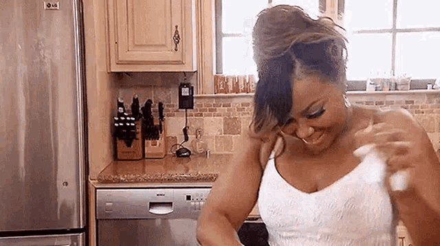 a woman in a white dress is standing in a kitchen with a dishwasher and refrigerator .