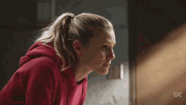 a woman in a red hoodie is looking down with a uc logo in the background