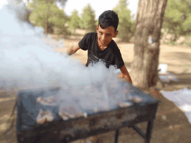 a boy in a black shirt is cooking on a grill with smoke coming out of it