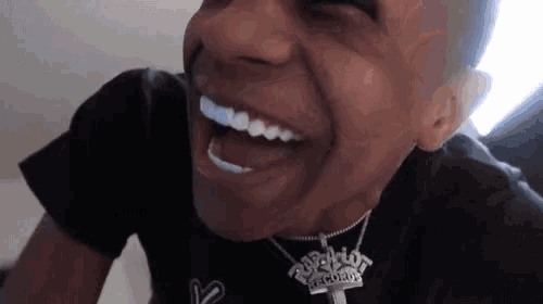 a man wearing a black shirt and a necklace with the word records on it is laughing