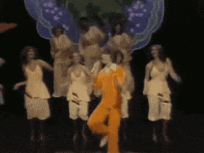 a man in a yellow suit is dancing in front of a group of women