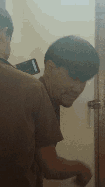 a man in a brown shirt is standing next to another man with a cell phone on his back
