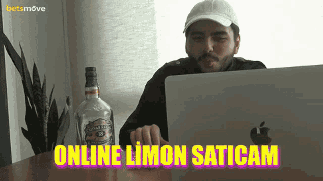 a man sitting at a table with a laptop and a bottle of chivas regal whisky