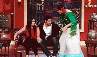 a man and a woman are sitting on a couch while a woman in a green dress stands between them