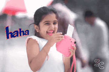 a little girl is laughing and holding a pink polaroid camera
