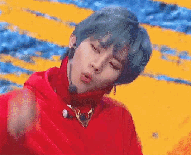 a young man with blue hair is wearing a red sweater and a microphone on his neck .