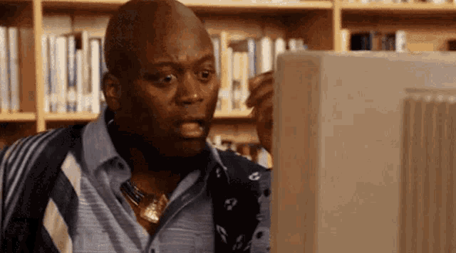 a man is looking at a computer screen in a library and making a surprised face .